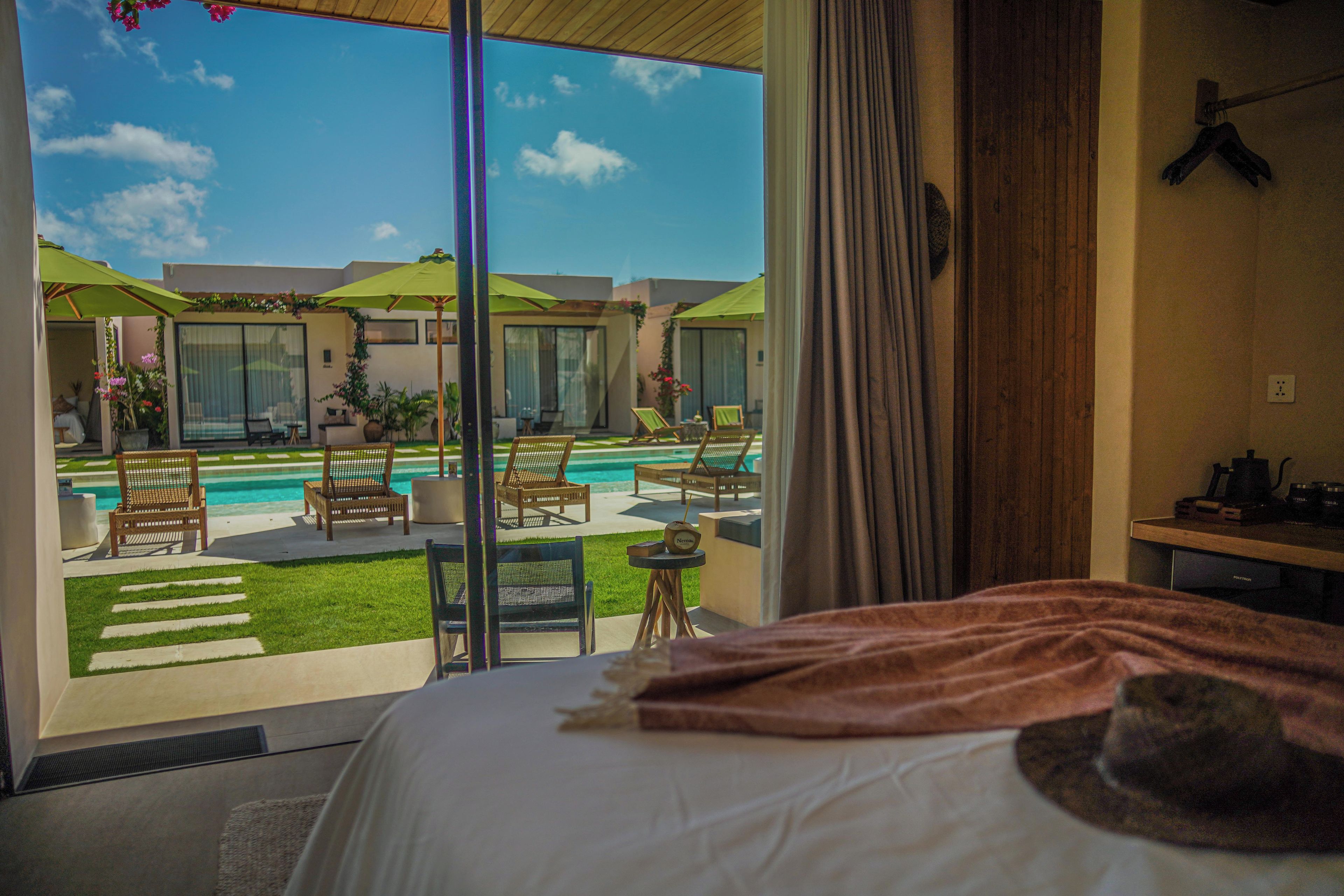 A hotel room with a large window overlooking a swimming pool and outdoor seating area.