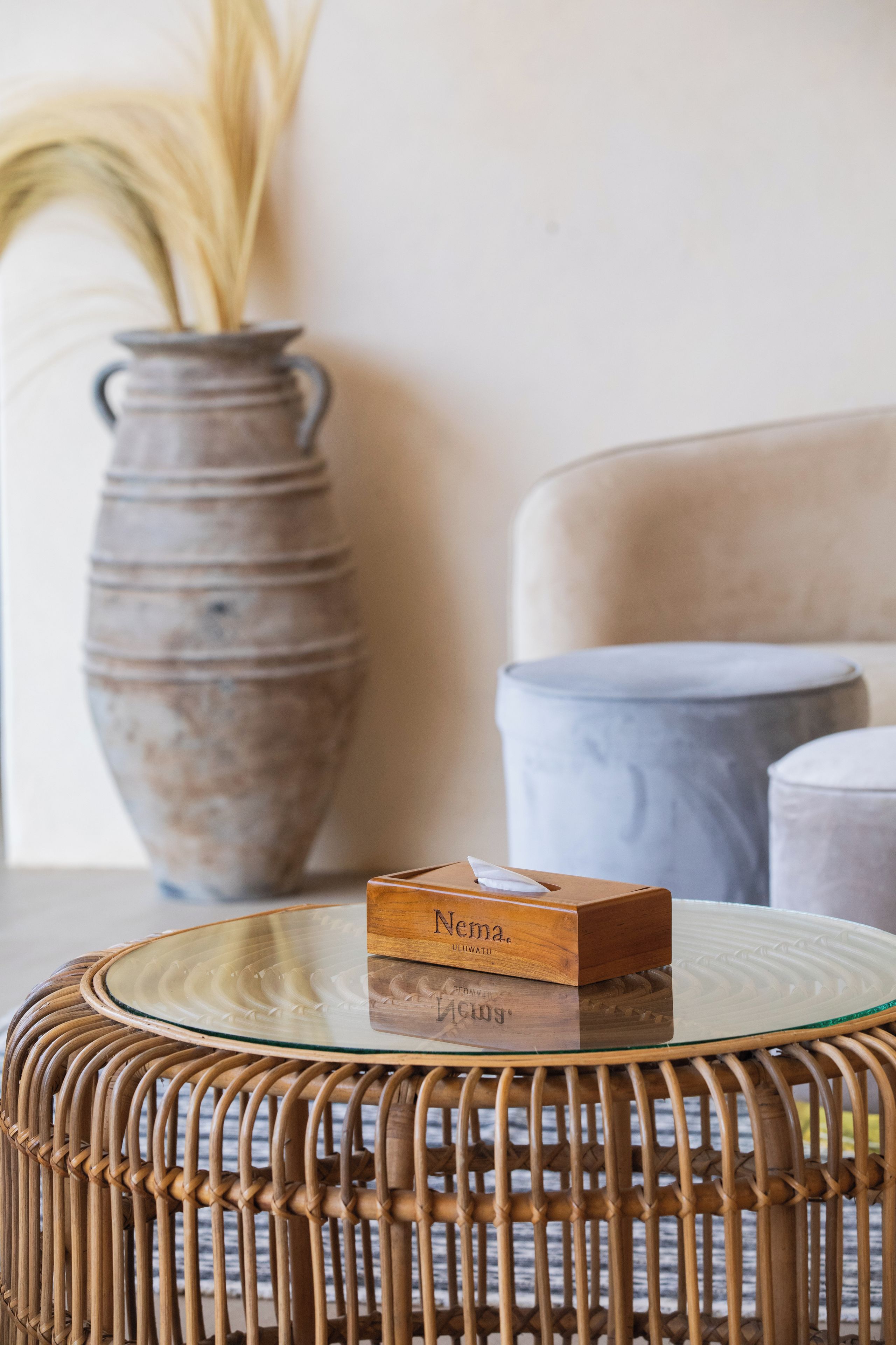 A wicker table with a glass top, a vase with dried plants, and a box labeled 'Neima.'