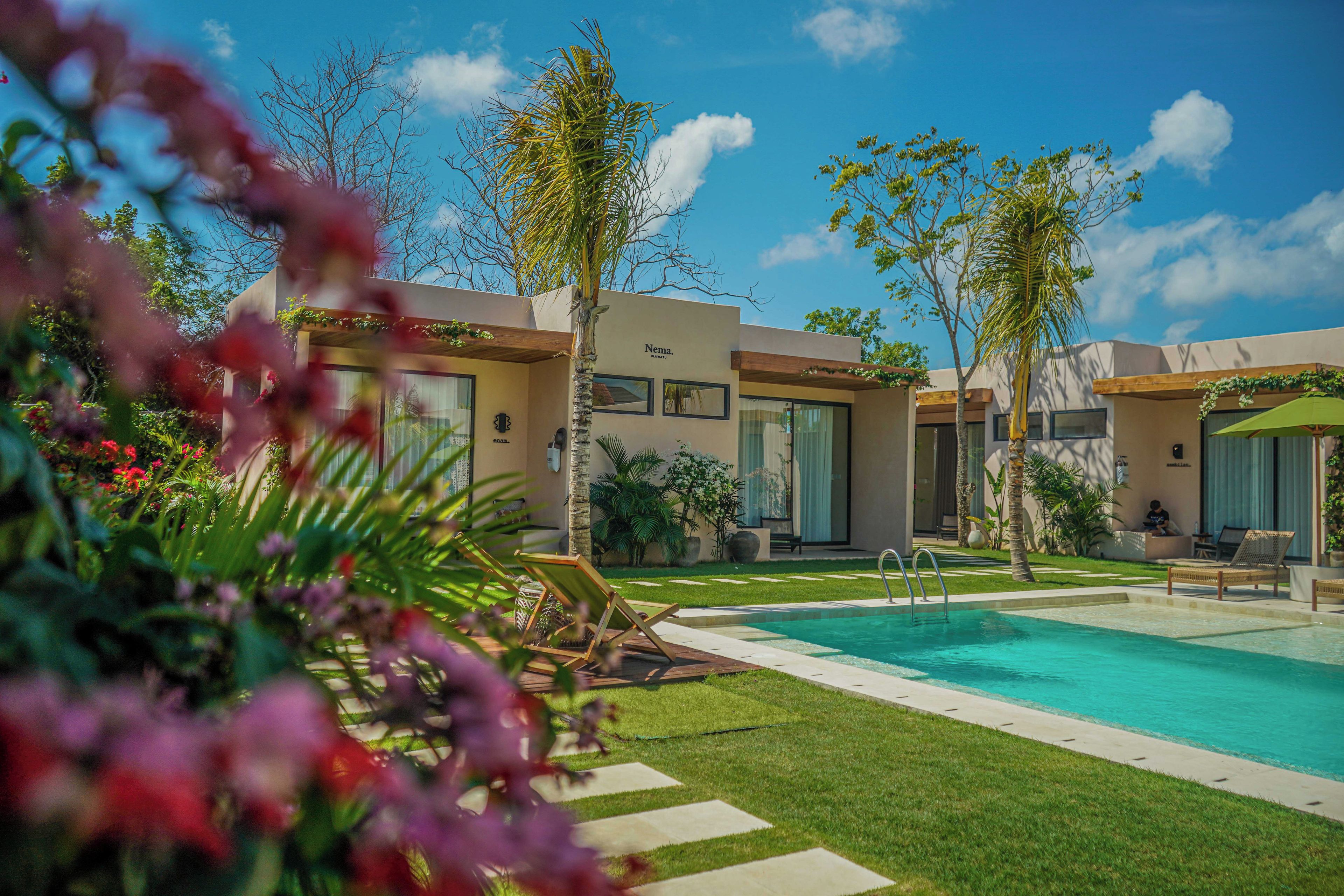 A modern resort with a swimming pool, lounge chairs, and a well-maintained garden.