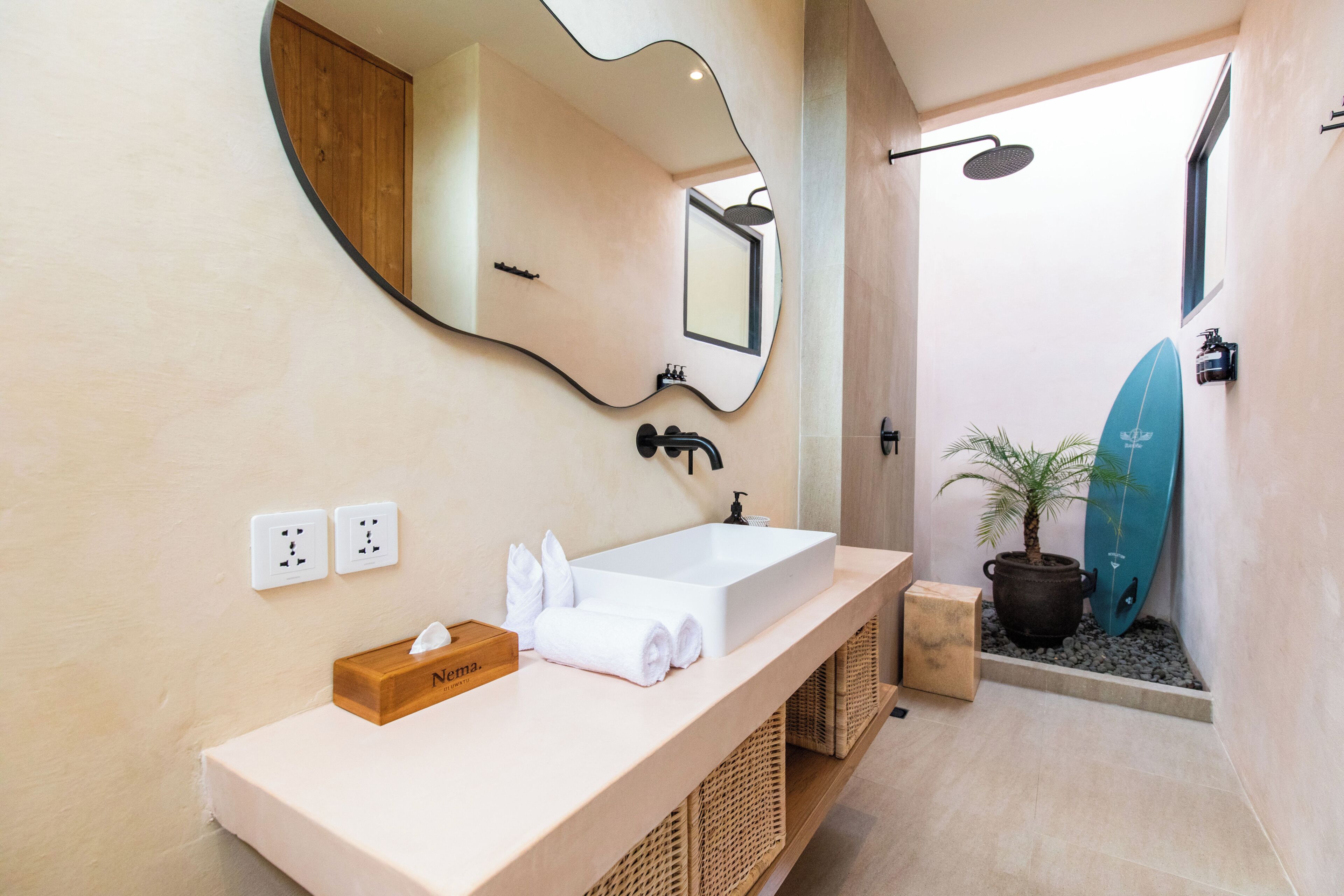 A bathroom with a large mirror, a sink, a towel rack, a shower, and a surfboard.