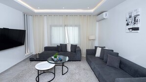 A modern living room with a grey sofa, a glass coffee table, and a flat-screen TV. - sandra 11 (La Marsa)
