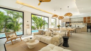 A modern living room with a large sofa, a dining area, and a kitchen. - Villa Malaikat (Canggu)