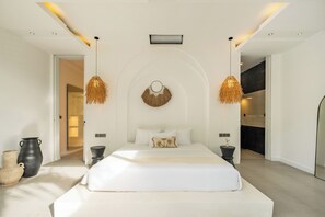 A modern bedroom with a large bed, two pendant lights, and a wall-mounted decorative item. - Villa Malaikat (Canggu)