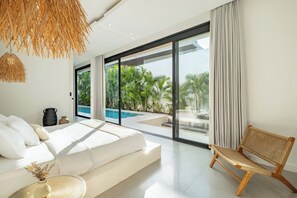 A modern bedroom with a large bed, a wicker chair, and a view of a swimming pool. - Villa Malaikat (Canggu)