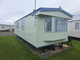 Une maison mobile dotée d’un toit plat, de deux fenêtres ornées de rideaux en dentelle et d’un petit porche.