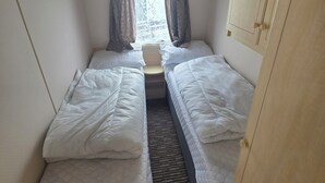A narrow room with two single beds, a window with curtains, and a wooden wardrobe.