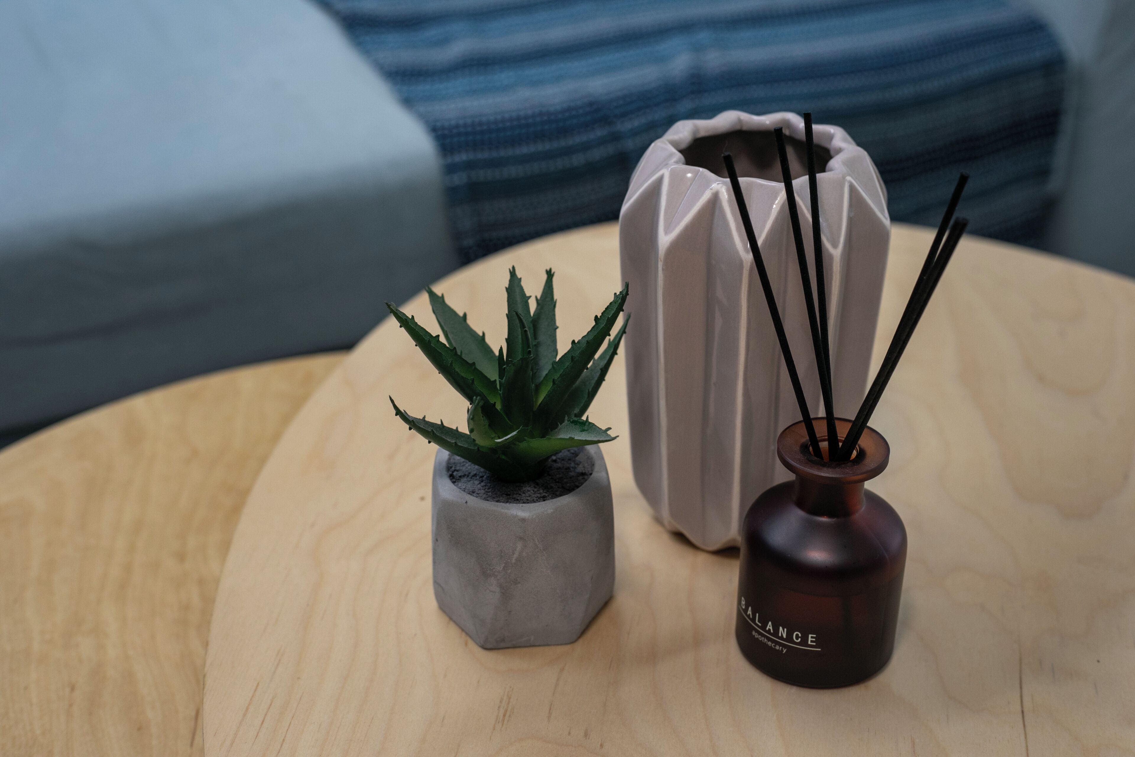 Een ronde houten tafel met een grijze plant in pot, een bruine fles met zwarte takken, en een witte vaas met zwarte takken.