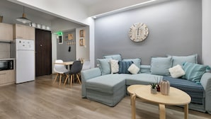 A modern living room with a sectional sofa, a round coffee table, and a kitchen area with a refrigerator and microwave. - City Vibes - 2-BR Apt. with Backyard in kolonaki (Athens)