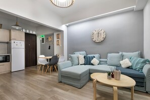 A modern living room with a sectional sofa, a round coffee table, and a kitchen area with a refrigerator and microwave. - City Vibes - 2-BR Apt. with Backyard in kolonaki (Athens)