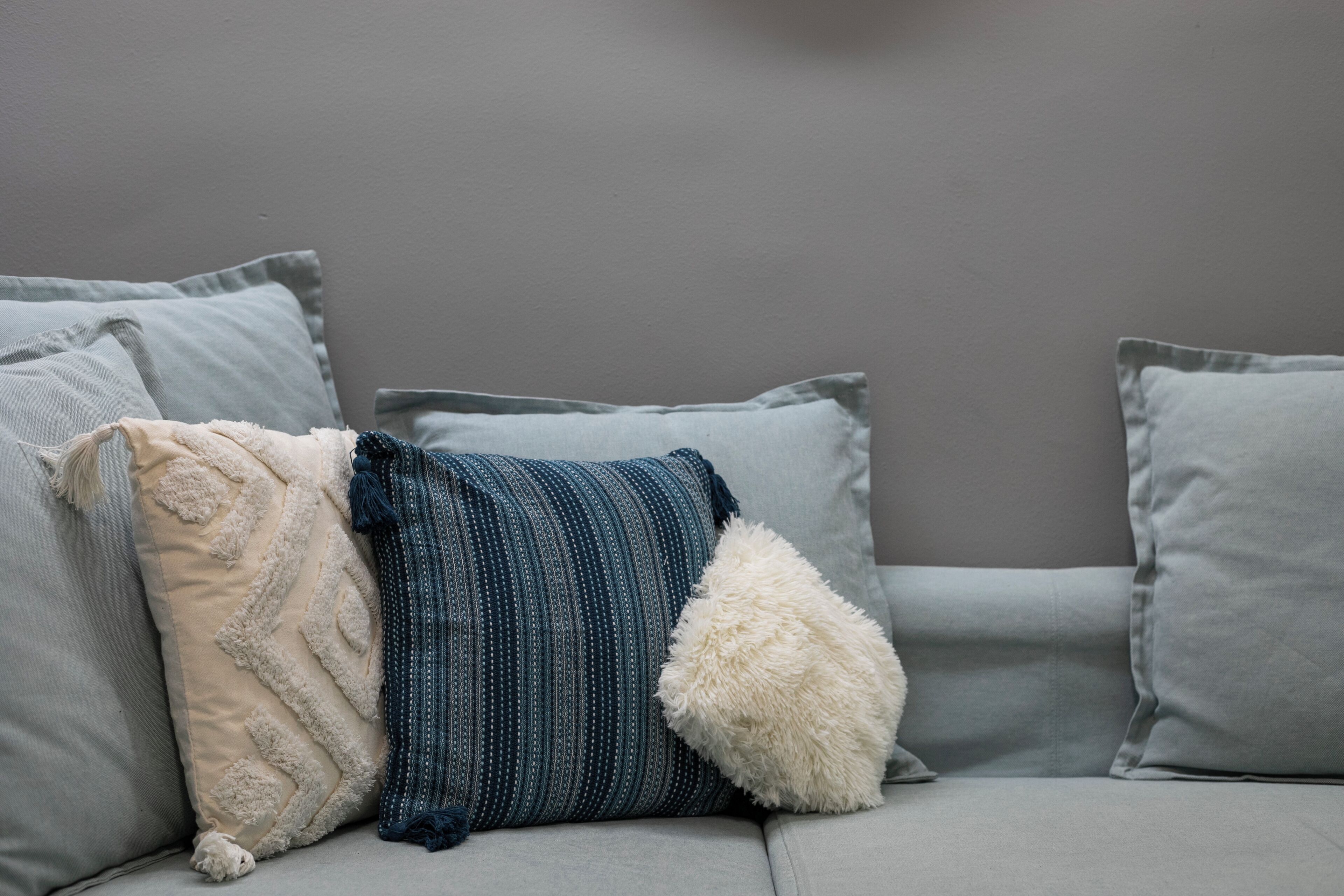 A grey sofa with three pillows of different textures and patterns.