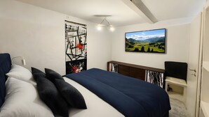 Ein Schlafzimmer mit Bett, Schreibtisch, Stuhl, einem Gemälde und Blick auf eine Landschaft.