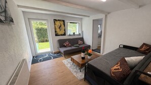 Ein modernes Wohnzimmer mit Sofa, Bett, Couchtisch mit Flasche und Blume sowie einem Bild an der Wand.