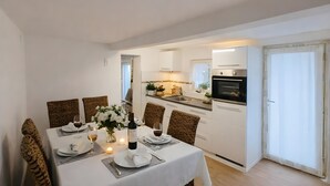 Ein Essbereich mit einem Tisch für zwei Personen, eine Küche im Hintergrund und eine Glasschiebetür zu einem Außenbereich.