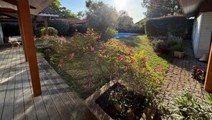 Una terraza de madera con vistas a un patio trasero, una piscina y un jardín con flores rosadas.