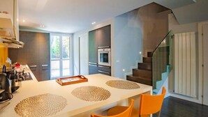 Una cocina moderna con una isla central, electrodomésticos integrados y una escalera que conduce a un nivel superior.
