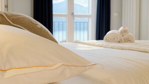 Una cama con ropa blanca y una almohada color beige, una ventana con vistas, y toallas enrolladas sobre la cama.