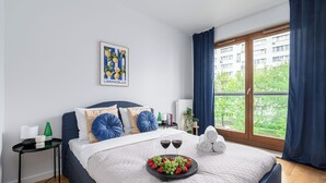 Une chambre à coucher avec un lit, une table de chevet, une fenêtre avec des rideaux et une vue sur la verdure à l’extérieur.