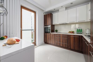 A modern kitchen with white cabinets, a built-in oven, and a window overlooking a balcony. - Lumina Apart near the Mall Fort Wola (Warsaw)