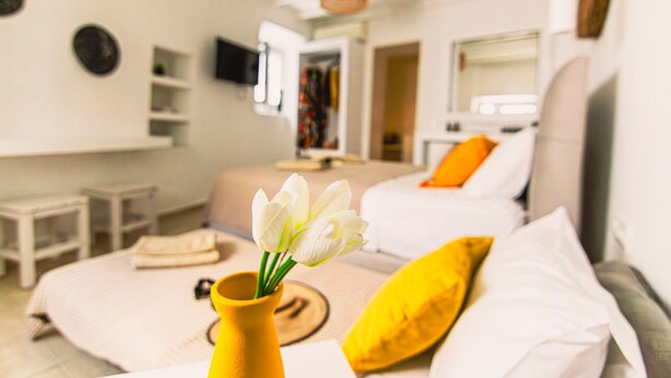 A bedroom with a bed, a bedside table, a vase with flowers, and a window. - Windmills Suite by Opus (Mykonos)