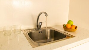 A kitchen sink with running water, two glasses, and a bowl of fruit. - Windmills Suite by Opus (Mykonos)