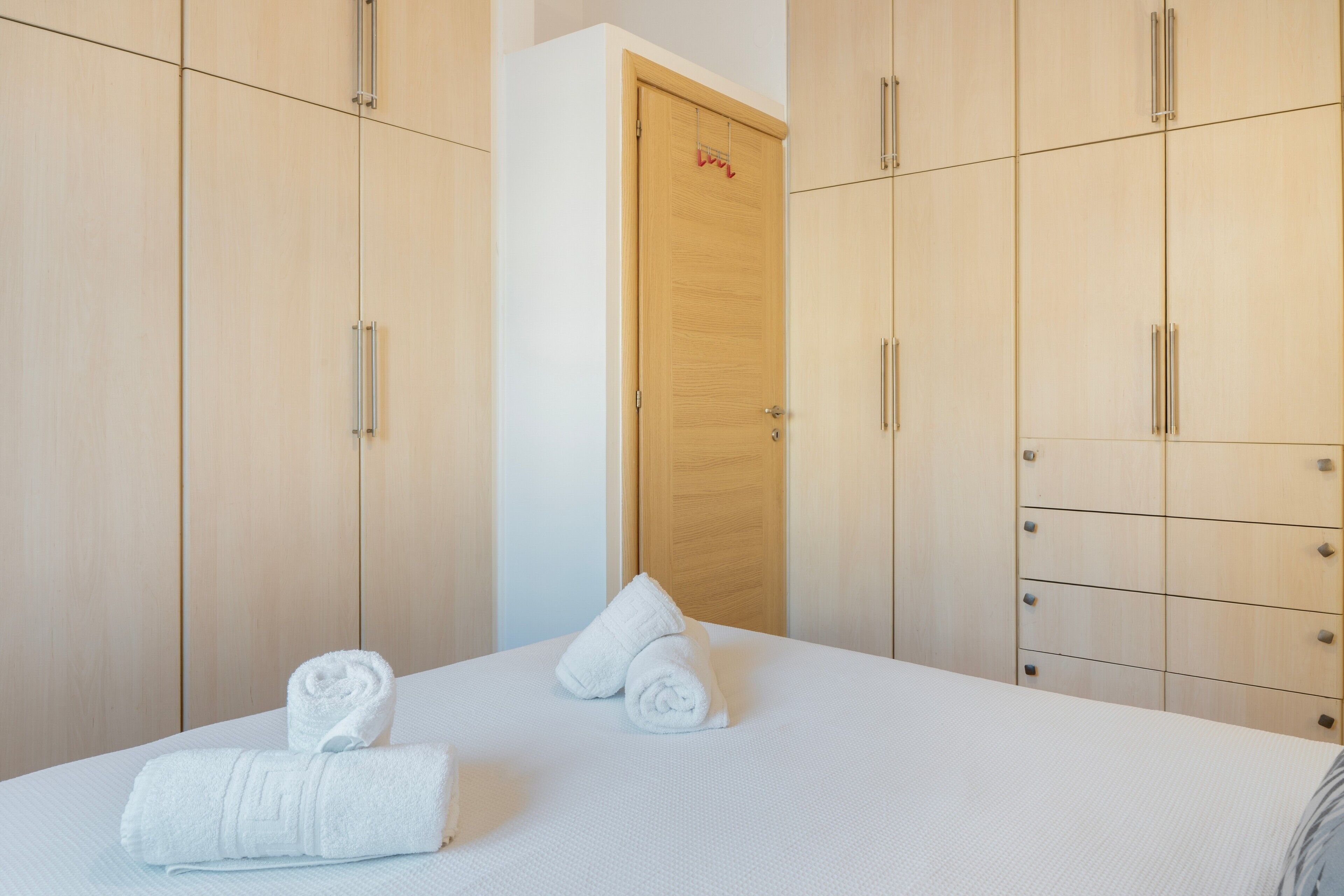 A hotel room with a bed, two rolled towels, and a wooden wardrobe with multiple drawers.