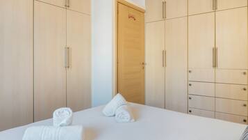 A hotel room with a bed, two rolled towels, and a wooden wardrobe with multiple drawers.