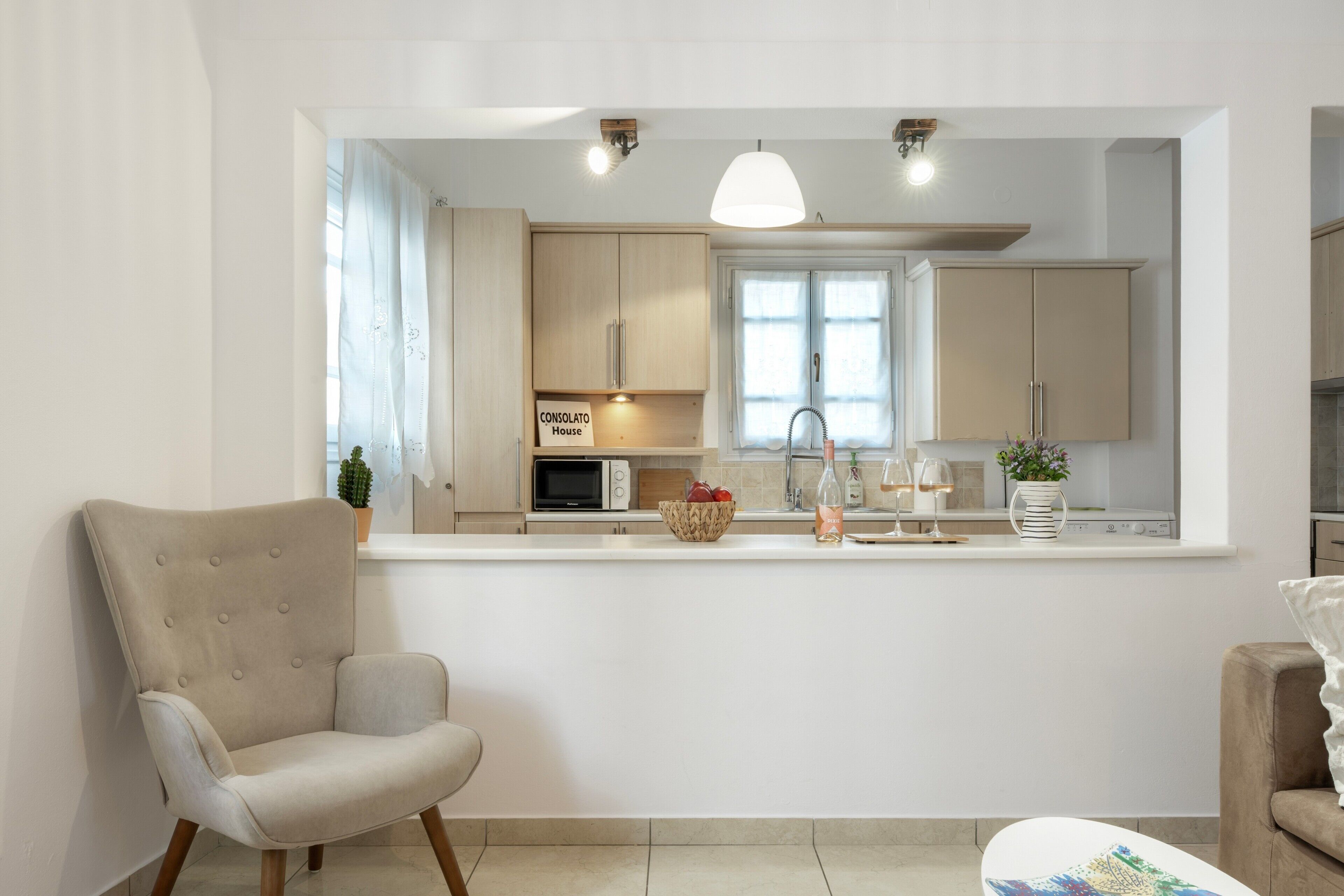 Una cuina moderna amb una illa central, una zona de menjador amb una cadira i un sofà.