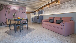 Un salon moderne avec un canapé rose, un coin repas avec une table et des chaises, et une cuisine équipée d’un four encastré.
