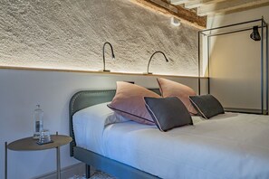 Ein ordentlich bezogenes Bett mit Kopfteil, ein Nachttisch mit Flasche und Glas sowie eine Wandleuchte.