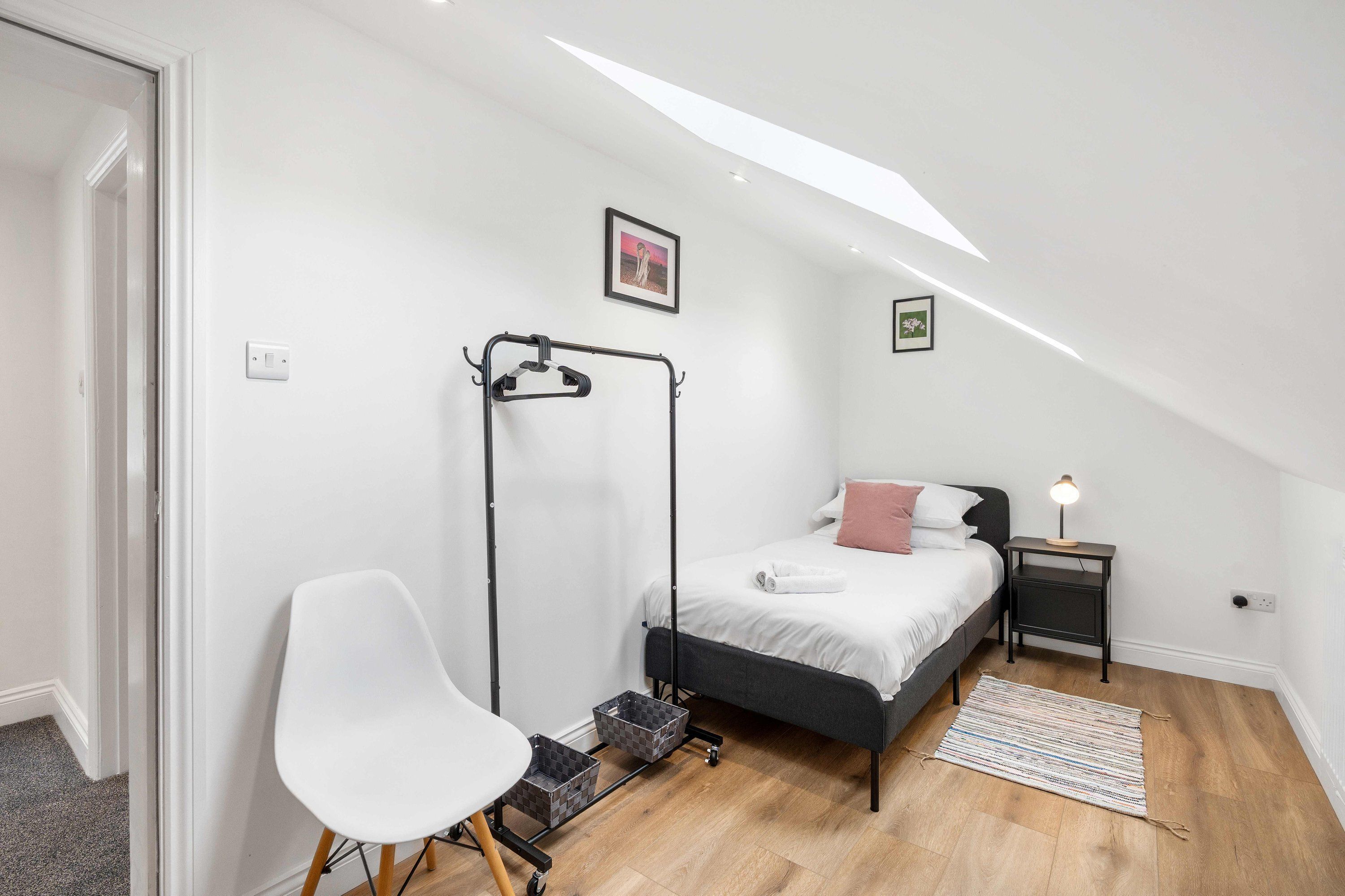 A bedroom with a bed, a chair, a small table, a nightstand, and a picture frame on the wall.
