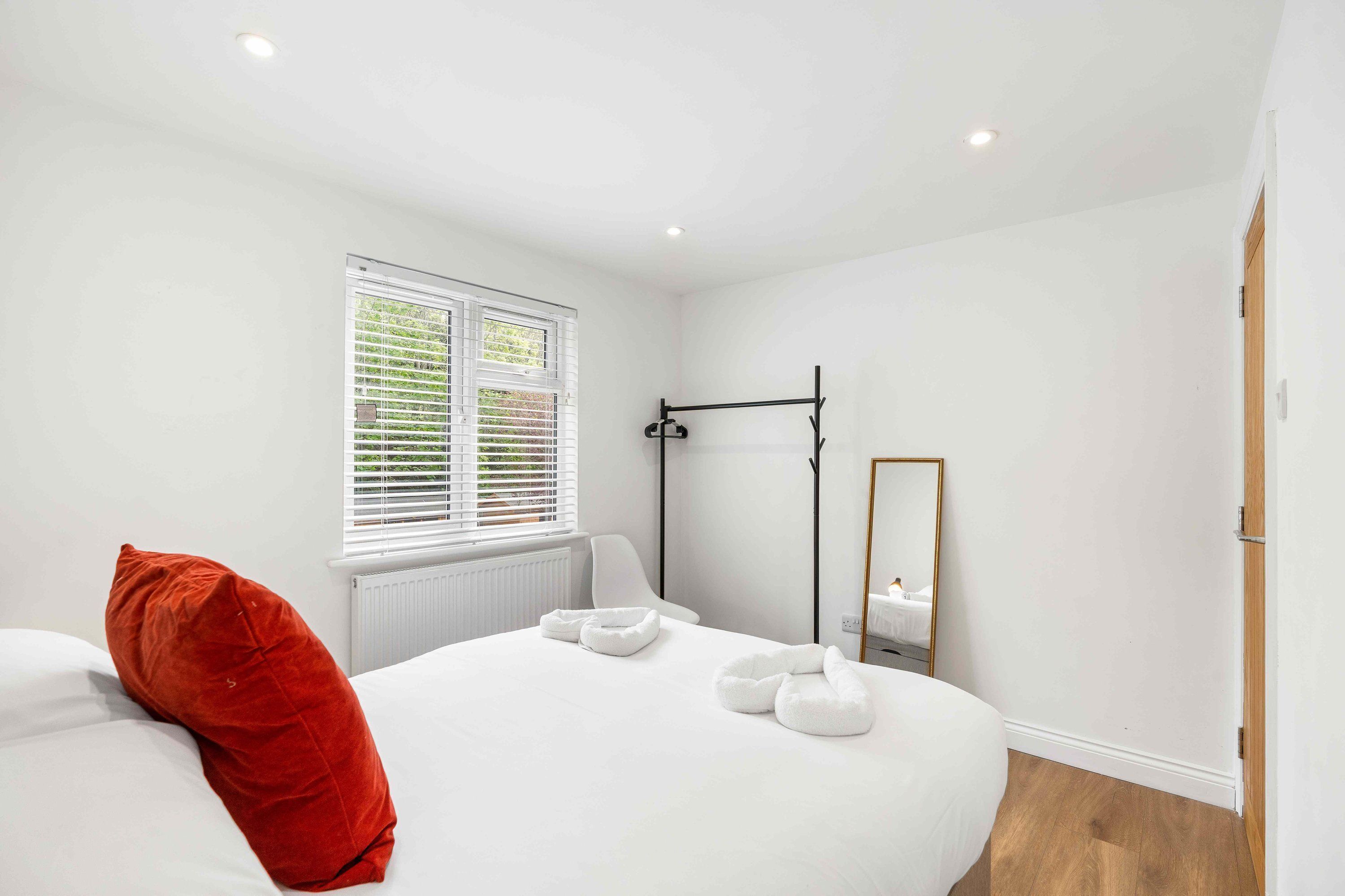 A bedroom with a bed, a window, a radiator, a mirror, and a door.