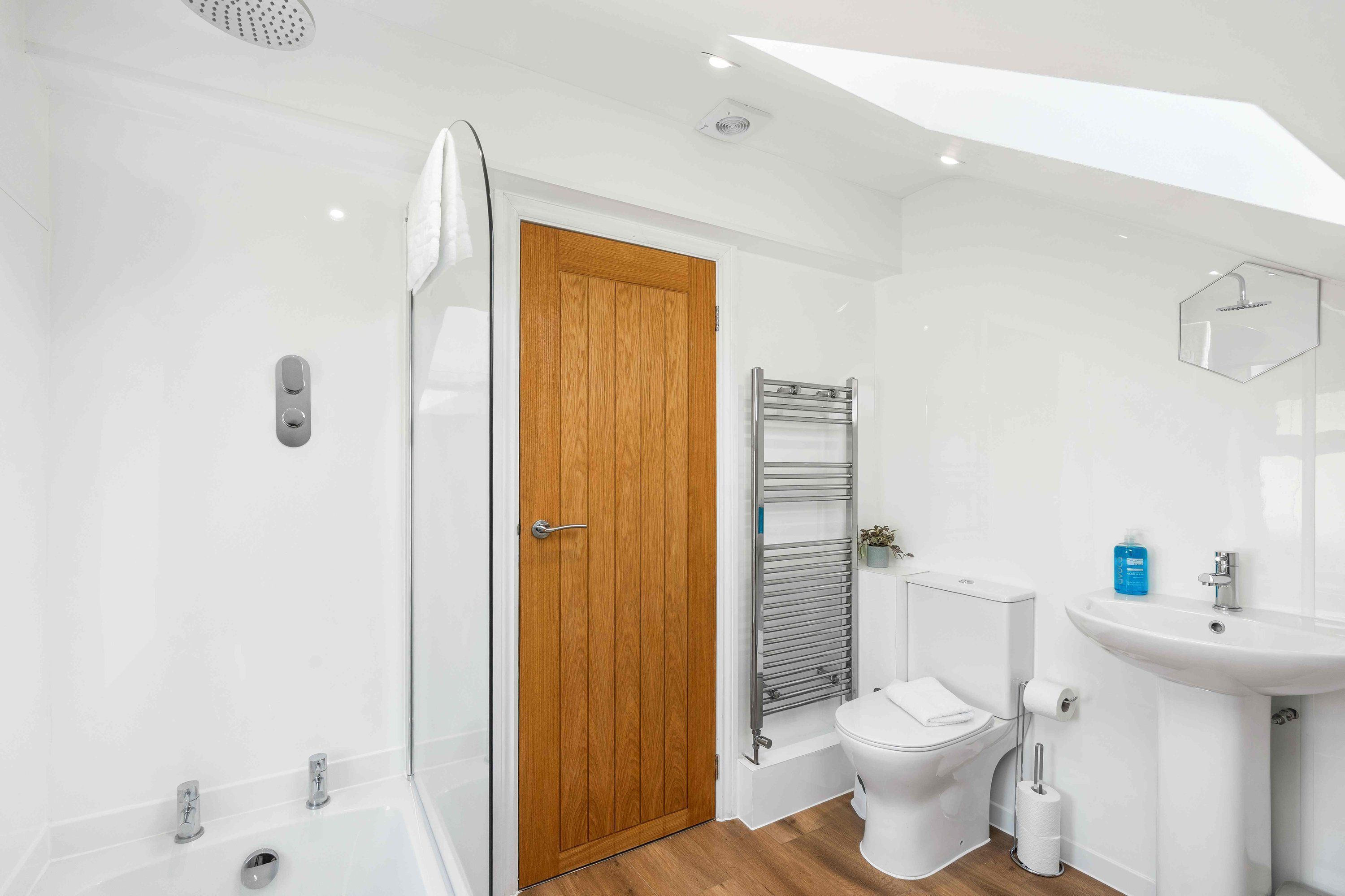 Een moderne badkamer met een houten deur, een douche, toilet en wastafel.