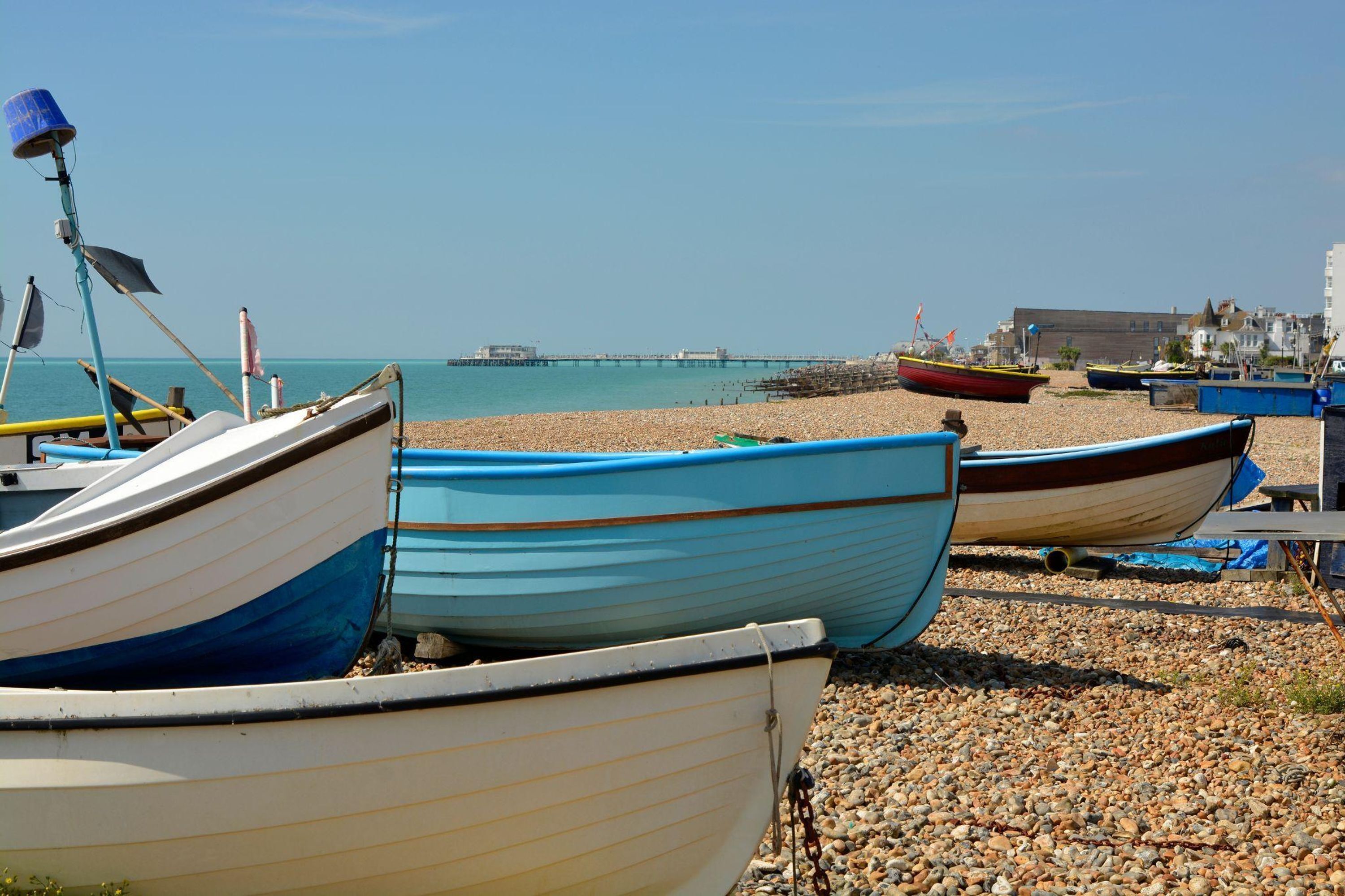 Boats docked on a pebbled beach with a pier in the background.