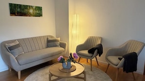 Un soggiorno moderno con un divano, due poltrone, un tavolino da caffè con fiori, una lampada da terra alta e un quadro appeso al muro.
