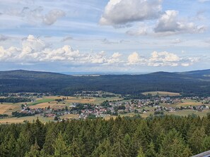 A panoramic view of a town surrounded by forests and hills, with a clear sky and scattered clouds.
