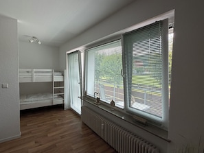 A room with a bunk bed, a radiator, and large windows with blinds. - Blum's Fichtelnest: Quiet, cozy apartment with 2 balconies and a view of the ski slopes (Mehlmeisel)