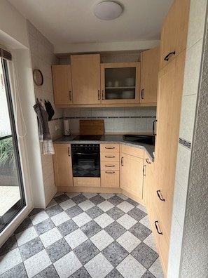 A kitchen with wooden cabinets, a black oven, and a checkered floor. - Blum's Fichtelnest: Quiet, cozy apartment with 2 balconies and a view of the ski slopes (Mehlmeisel)