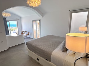 A bedroom with a bed, a lamp, a view through a door, and a dining area with a table and chairs. - Villa Kora (Episkopi Gonias)