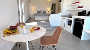Een moderne keuken met witte kasten, een eettafel met rieten stoelen, en een ontbijtgedeekte tafel met fruit en sap.
