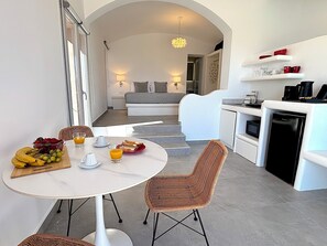 A modern kitchen with white cabinetry, a dining table with wicker chairs, and a breakfast setup with fruits and juice. - Villa Kora (Episkopi Gonias)