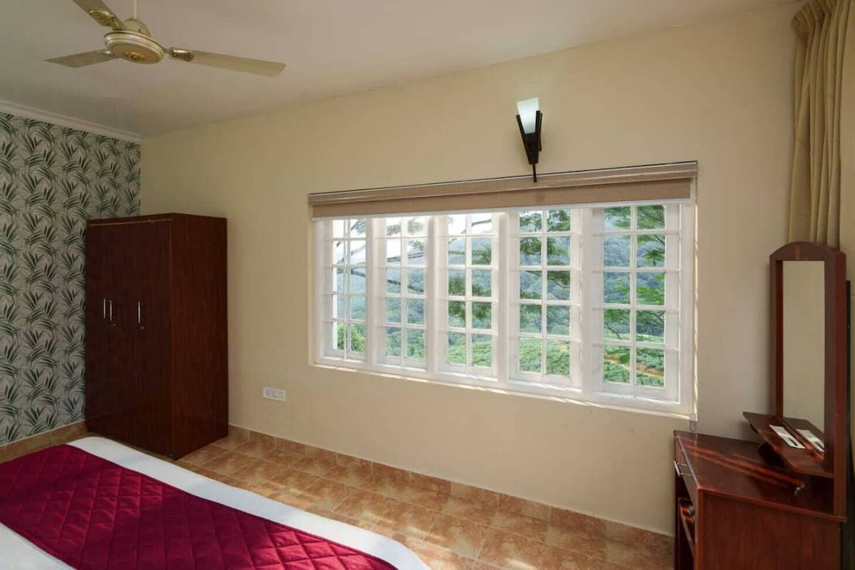 A bedroom with a bed, a wardrobe, a window with a view, and a ceiling fan.