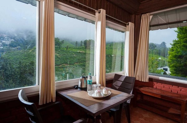 A room with a table set for breakfast, a bench, and a view of a hilly landscape.