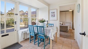 A dining area with a table set for two, a kitchen in the background, and a view of the outside. - 5 Courtyard Cottages - North East Escapes (Embleton)