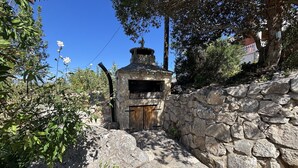 Edifício de pedra com porta de madeira, rodeado por vegetação e uma parede de pedra.
