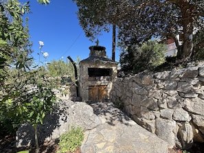 Un edificio de piedra con puerta de madera, rodeado de vegetación y un muro de piedra.