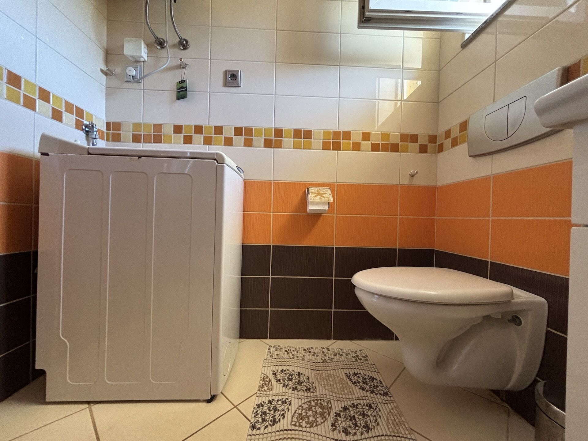 Ein Badezimmer mit Waschmaschine, Toilette, einem gemusterten Teppich und gefliesten Wänden.
