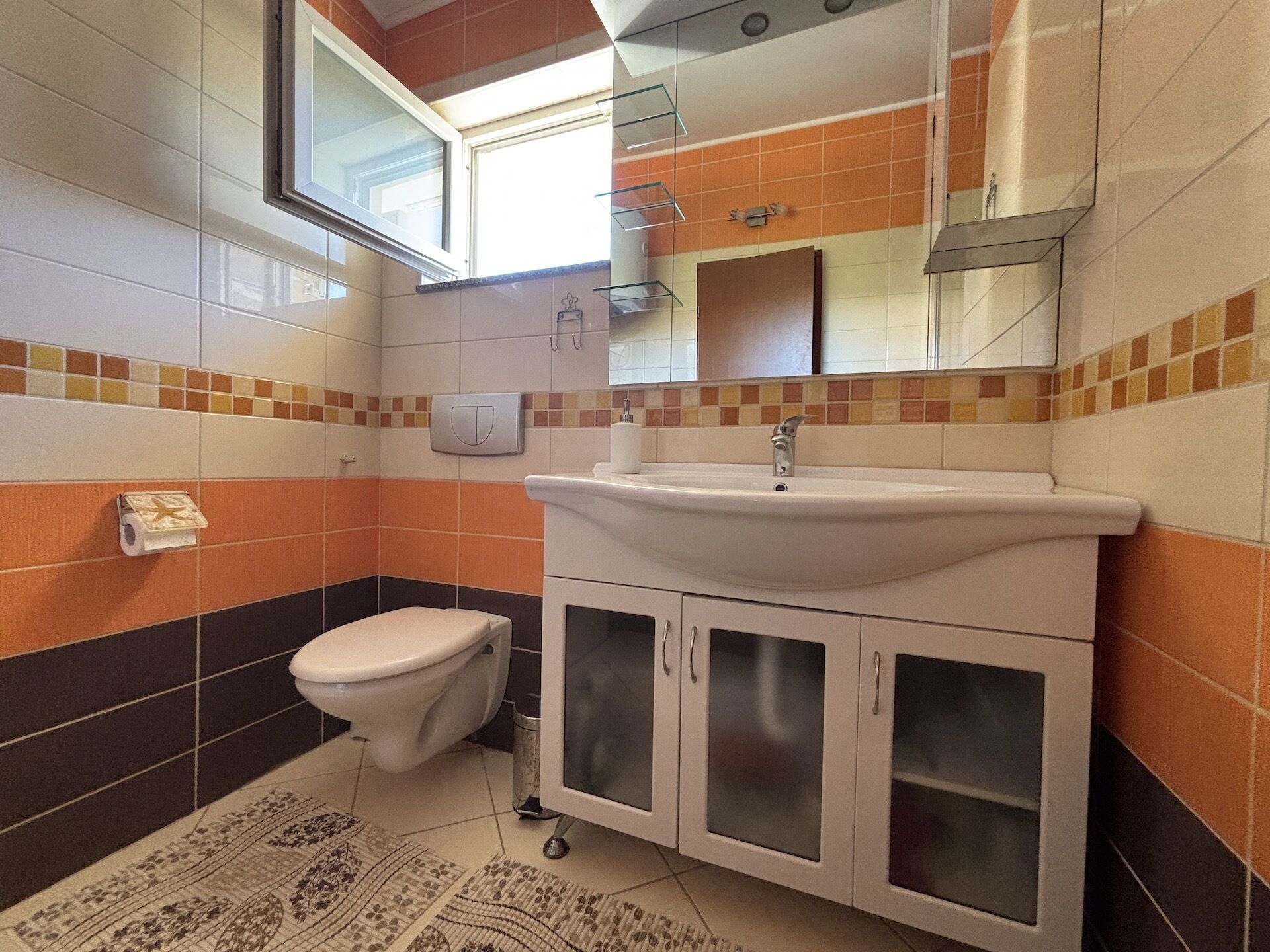 A bathroom with a toilet, sink, and cabinets.
