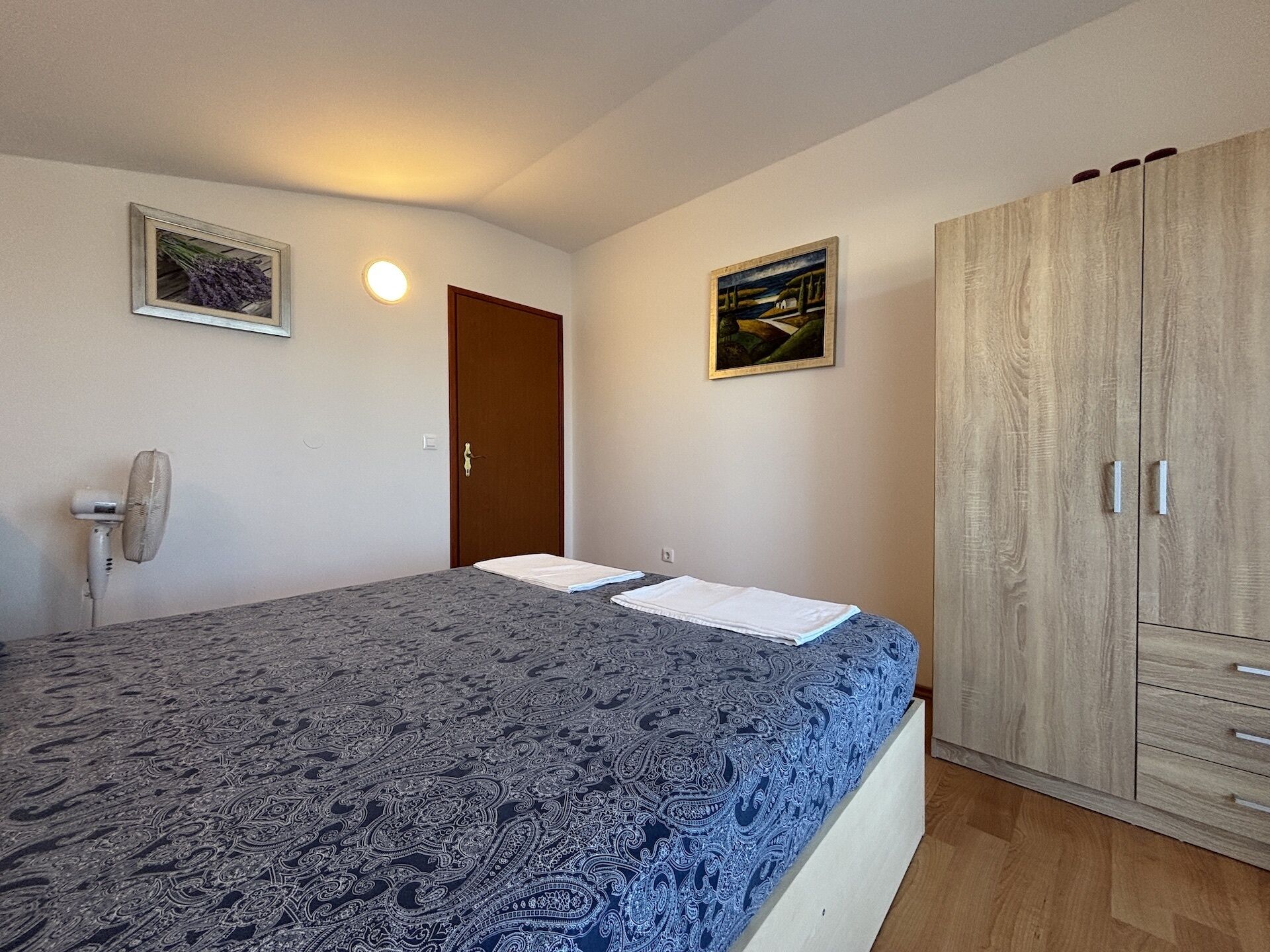 Ein Schlafzimmer mit einem Bett, einem Kleiderschrank, einer Tür und zwei Bildern an der Wand.