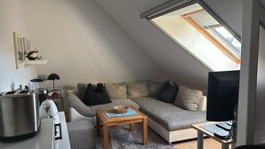 A loft-style living room with a sloped ceiling, a sofa, a coffee table, a television, and a kitchenette area. - Apartment 'Ferienwohnung Hühnergott' with Wi-Fi (Sassnitz)