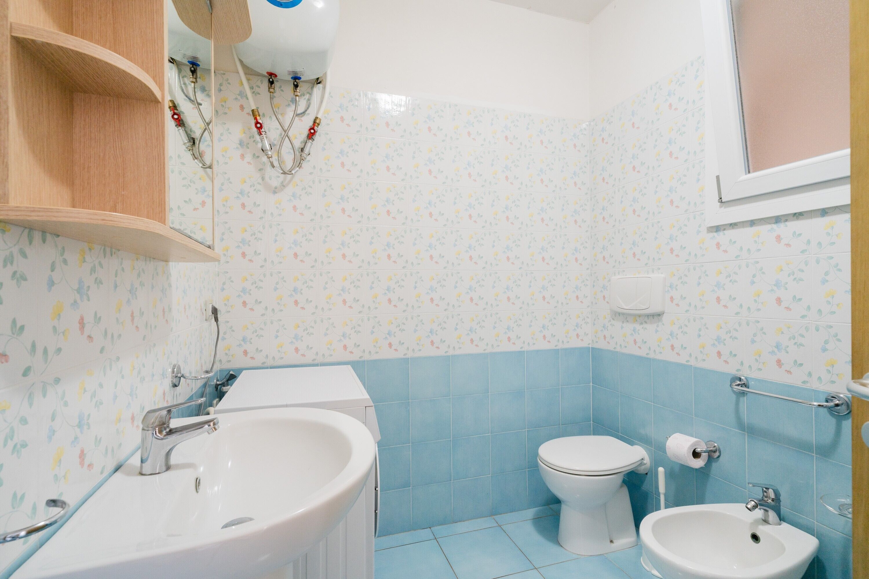 A bathroom with a sink, toilet, and bidet, tiled in blue and white floral patterns.